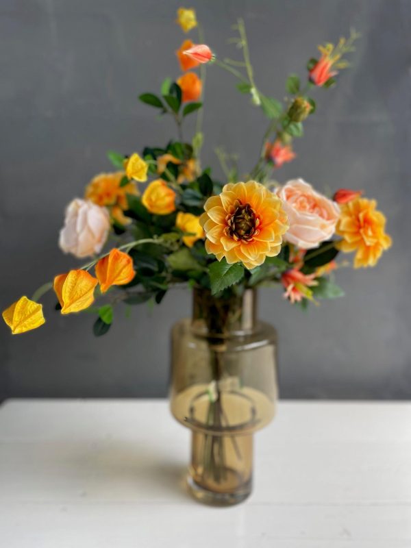 Heldere oranje dahlia met perzikkleurige rozen en physalis in een vaas